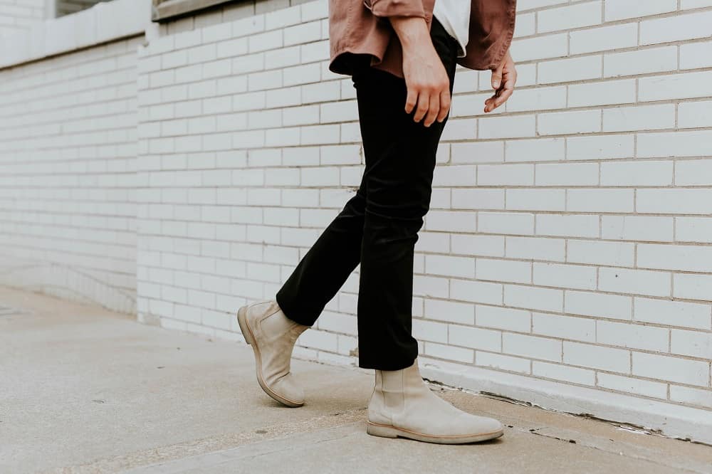 shot of a mans legs walking down the street, wearing black jeans and cream-colored Chelsea boots