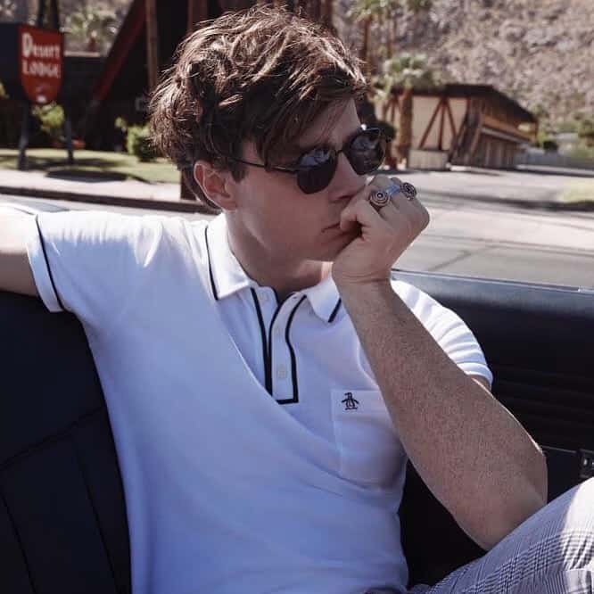A young man sitting in a car wearing a white Original Penguin polo shirt