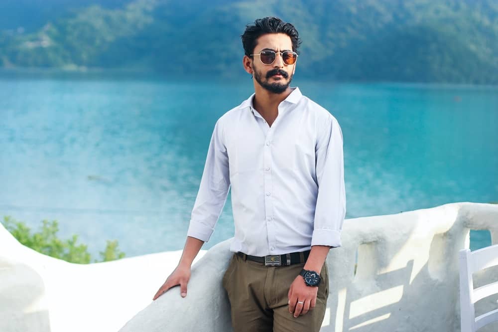man stands beside a body of water, wearing khakis and a fitted button up shirt