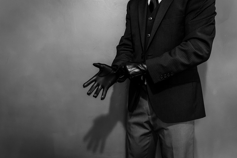 A person in a suit adjusts a black glove on their right hand