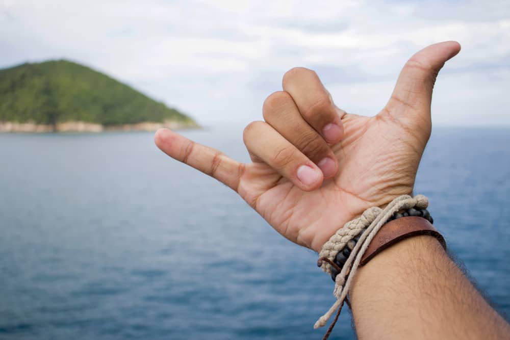 A man giving the shaka sign while wearing leather and hemp bracelets