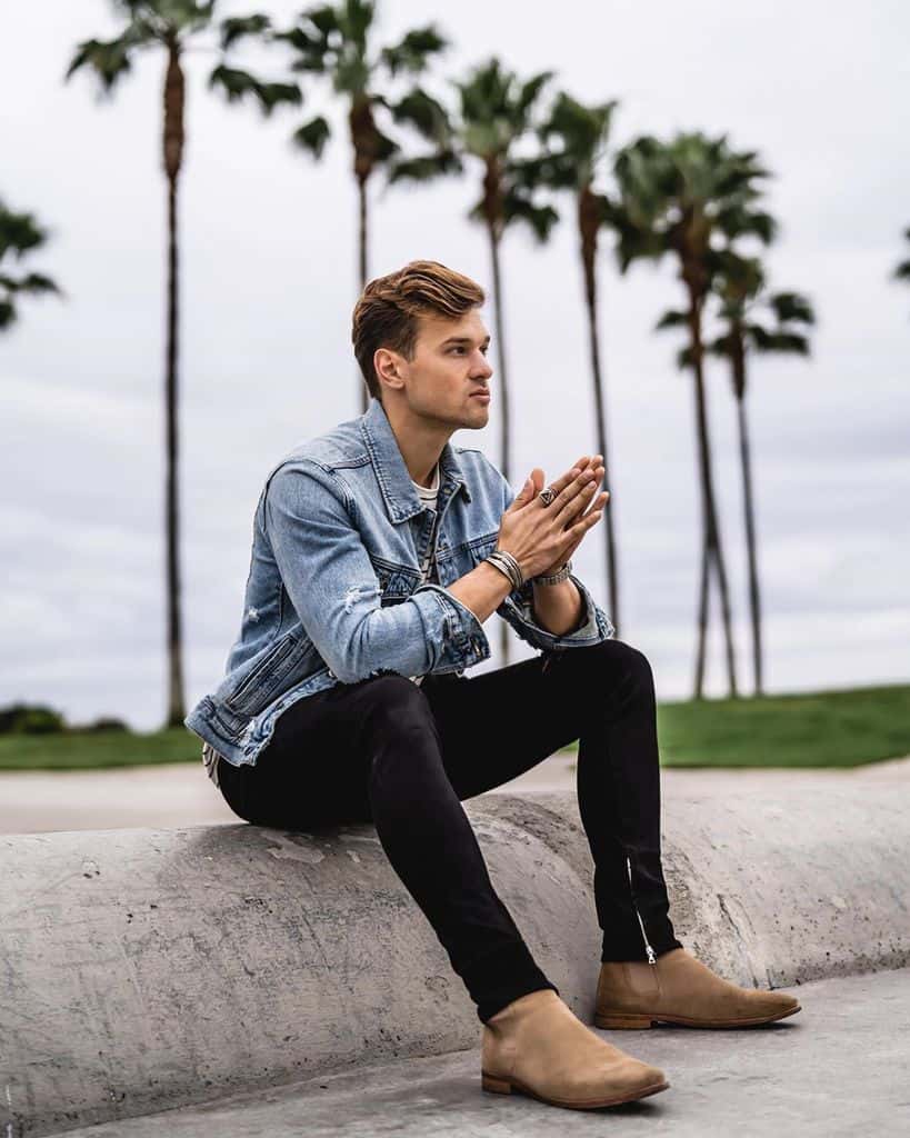 A man sitting outside wearing tan Chelsea boots under black jeans