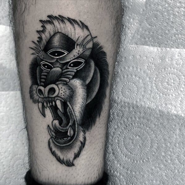 Black and grey baboon tattoo with bold shading, fierce expression, and a mystical third eye, creating a striking and surreal leg design.