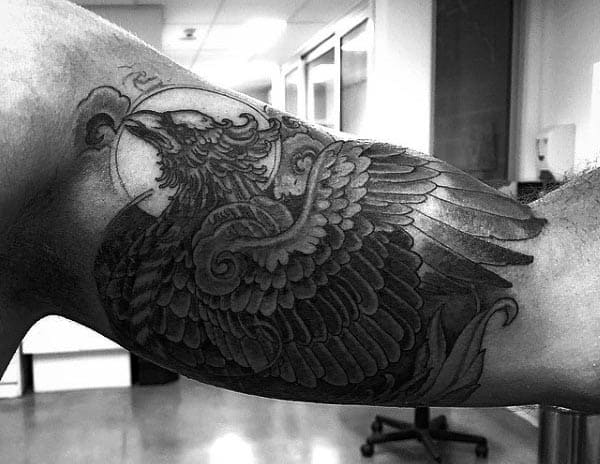 Black and grey tattoo of a majestic eagle with detailed feathers and a fierce expression, covering the inner bicep with bold shading