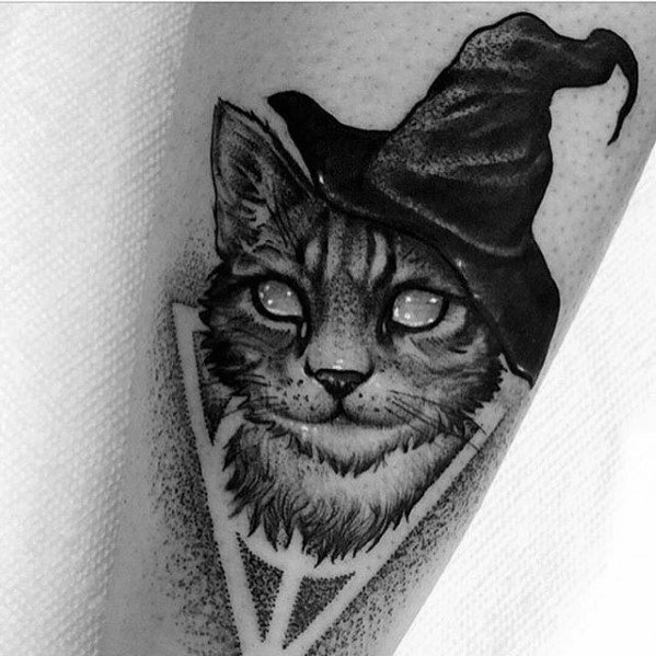 Blackwork tattoo of a mystical cat wearing a witch hat, featuring fine details and a geometric frame for an enchanting design.