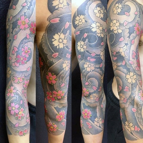 Japanese-style full sleeve tattoo featuring intricate cherry blossoms with soft pink petals, swirling wind patterns, and bold black shading