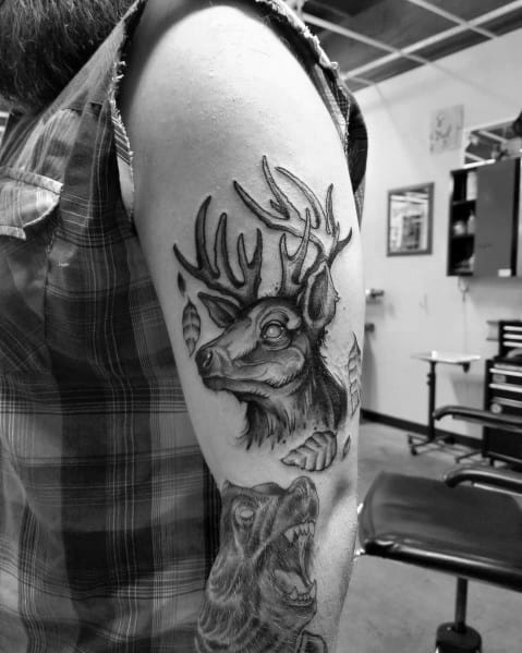 Realistic black and grey elk and bear tattoo on the upper arm, featuring fine shading and bold details for a powerful wildlife-inspired design.