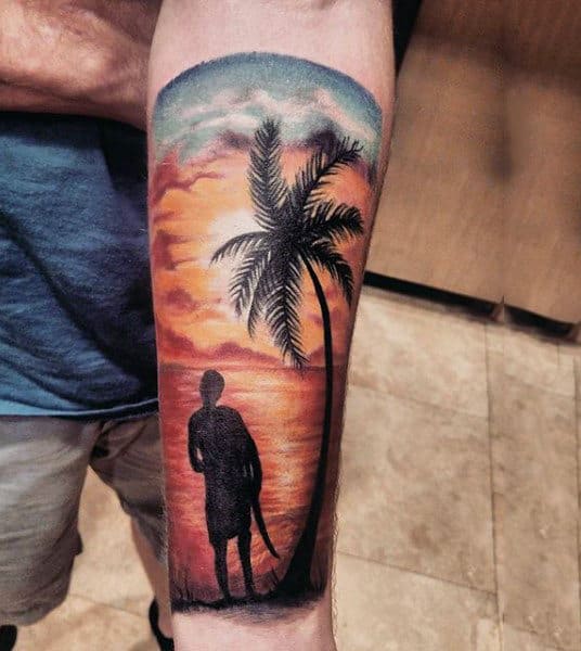 Man With Forearm Tattoo Of Man At Sunset Beach
