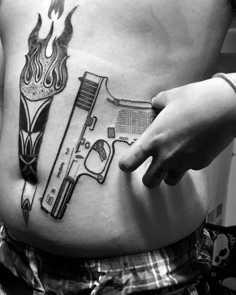 Black and grey tattoo of a Glock pistol on the lower abdomen, positioned to align with the hand for a creative and interactive design effect.