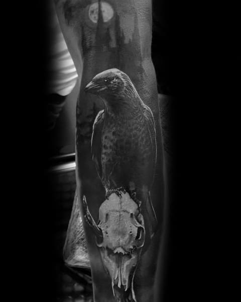 Gothic black and grey tattoo featuring a raven perched on an animal skull, with a full moon and eerie castle silhouette in the background.