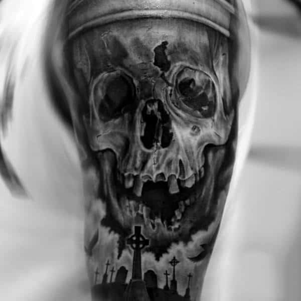 A haunting black and white tattoo featuring a skull intertwined with a graveyard scene on an upper arm