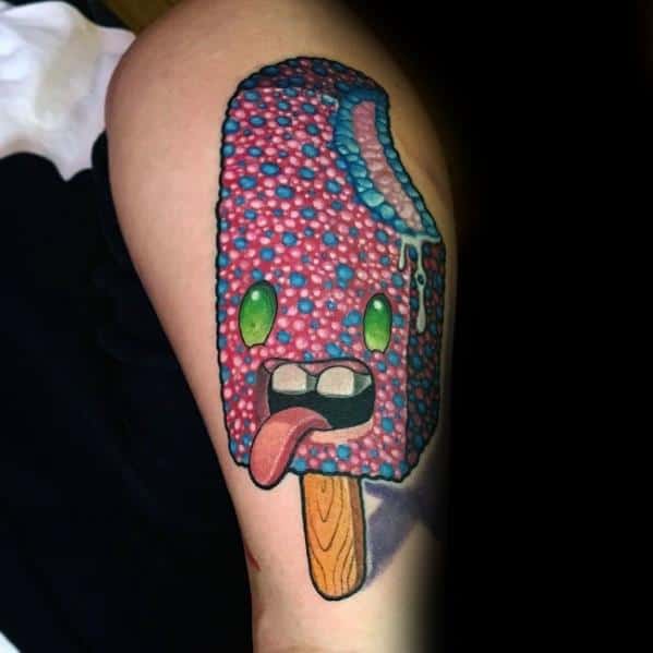 Colorful tattoo of a textured, candy-coated popsicle with glowing green eyes, a playful tongue, and a melting bite mark, blending fun and surreal elements.