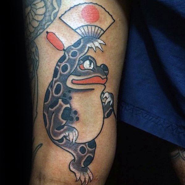 Japanese-style tattoo featuring a black-spotted frog holding a traditional folding fan with a red sun design, symbolizing grace, culture, and folklore.