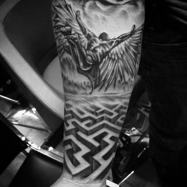 Realistic black and grey tattoo on a man's forearm, featuring Icarus falling above a 3D labyrinth, symbolizing mythology and fate.