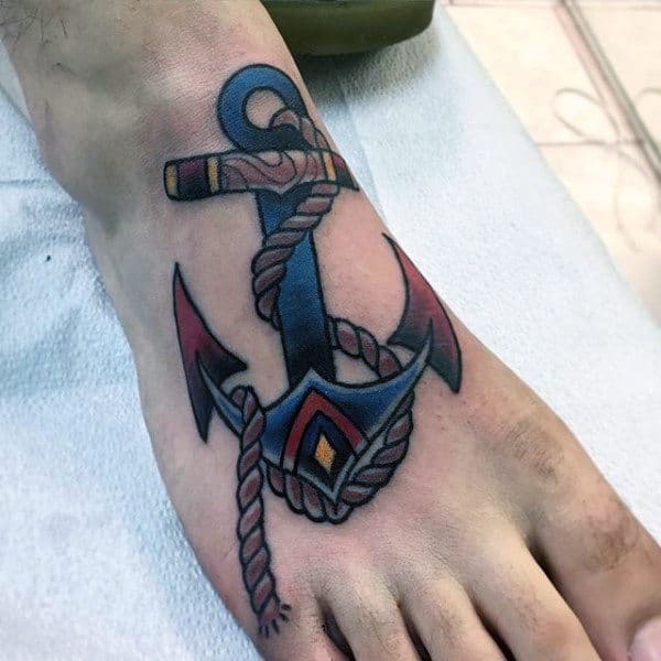 Tattoo of an anchor with rope, colored in blue and red, located on the top of a foot