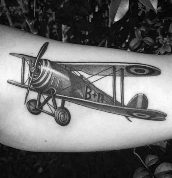Black and grey forearm tattoo of a vintage biplane with fine linework, shading, and detailed propeller, capturing a classic aviation style.