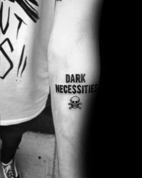 Minimalist forearm tattoo with bold "Dark Necessities" lettering and a small skull and crossbones, inspired by the Red Hot Chili Peppers.