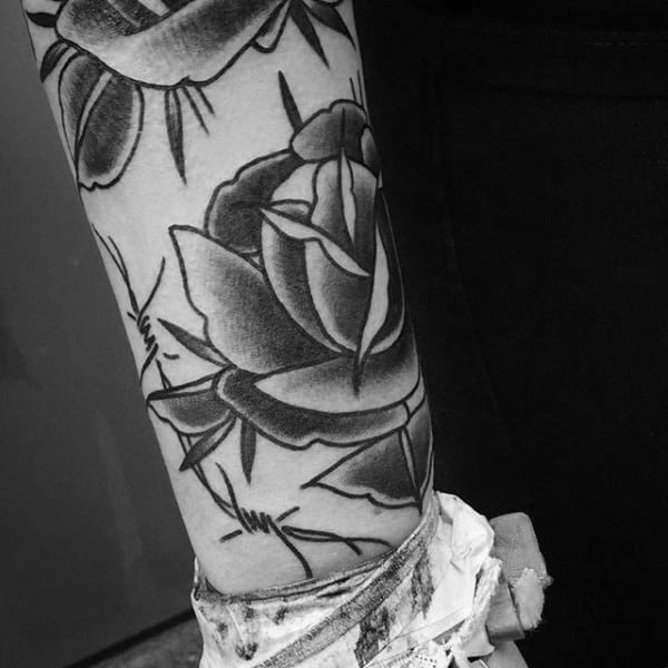 Man With Sailor Jerry Rose Flowers And Barbed Wire Tattoo Design On Arm