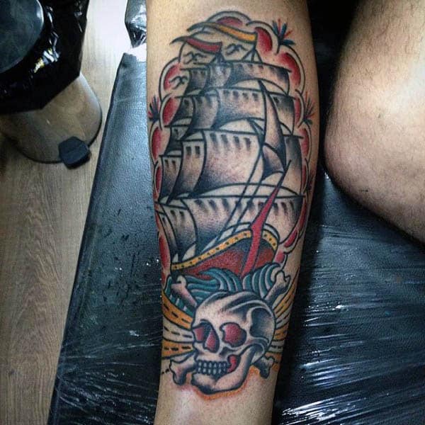Man With Sailor Jerry Themed Sailboat And Skull Tattoo On Inner Forearm
