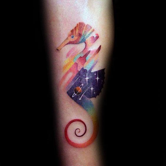 Watercolor galaxy seahorse tattoo on forearm, featuring soft pastel hues blending into a cosmic design with stars and a planet for a dreamy effect.