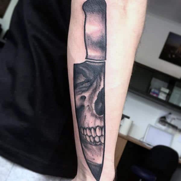 Man With Skull Chef Knife Tattoo On Outer Forearm