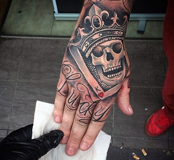 Man With Smiling Skull And Crown Tattoo On Hand