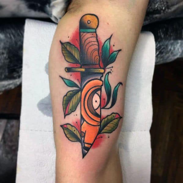 Neo-traditional tattoo of a dagger with Kenny’s hood design from South Park, featuring bold colors, leaves, and a red background splash.