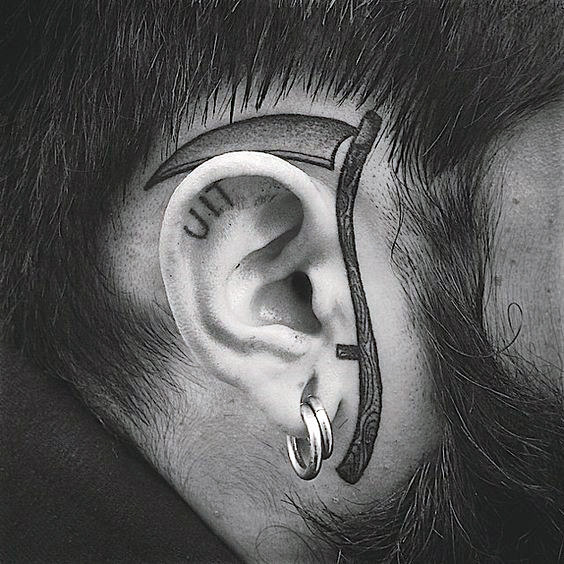 Man With Tattoo Of Scythe Around Ear On Face