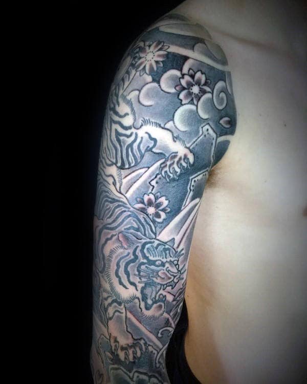 Japanese-style sleeve tattoo featuring a fierce tiger climbing rocky terrain, surrounded by cherry blossoms, swirling clouds, and bold shading