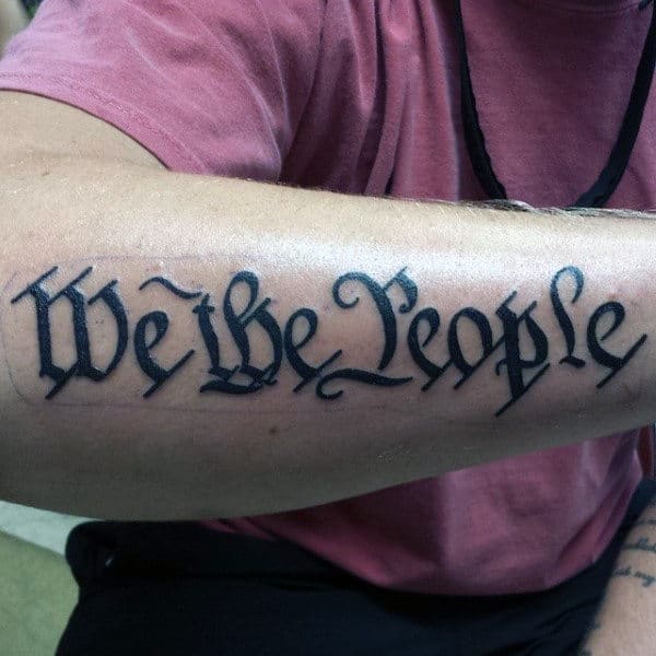 Man With We The People Black Ink Forearm Tattoo
