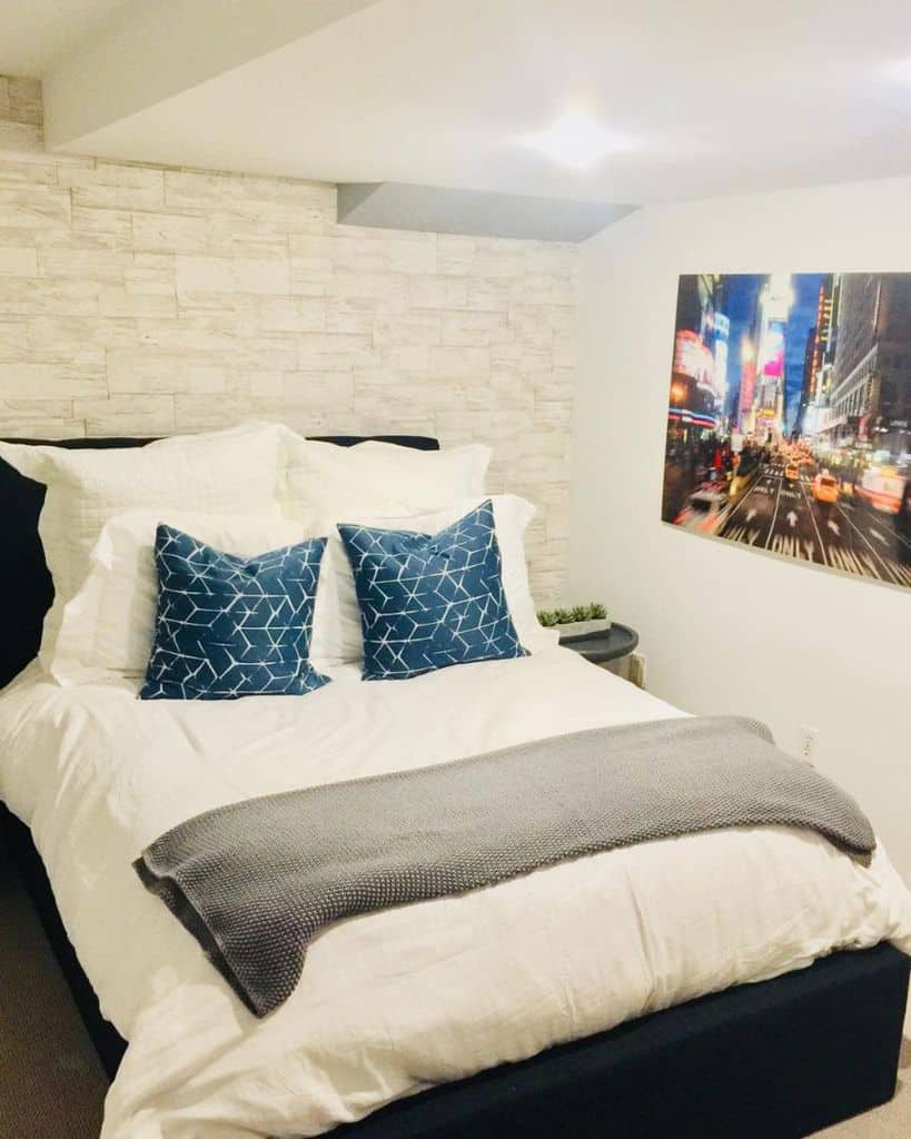 Small bedroom with blue accent pillows, stone accent wall, and cityscape wall art.