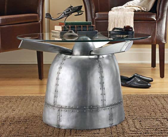 Glass table with a metal airplane engine base, small plane model on top, surrounded by leather chairs