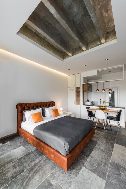 The ceiling features a modern, industrial design with exposed beams and recessed lighting, enhancing the minimalist aesthetic of the bedroom