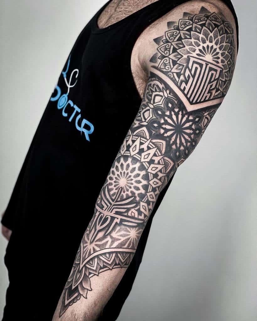 Arm with intricate black geometric tattoos in various patterns, extending from shoulder to forearm