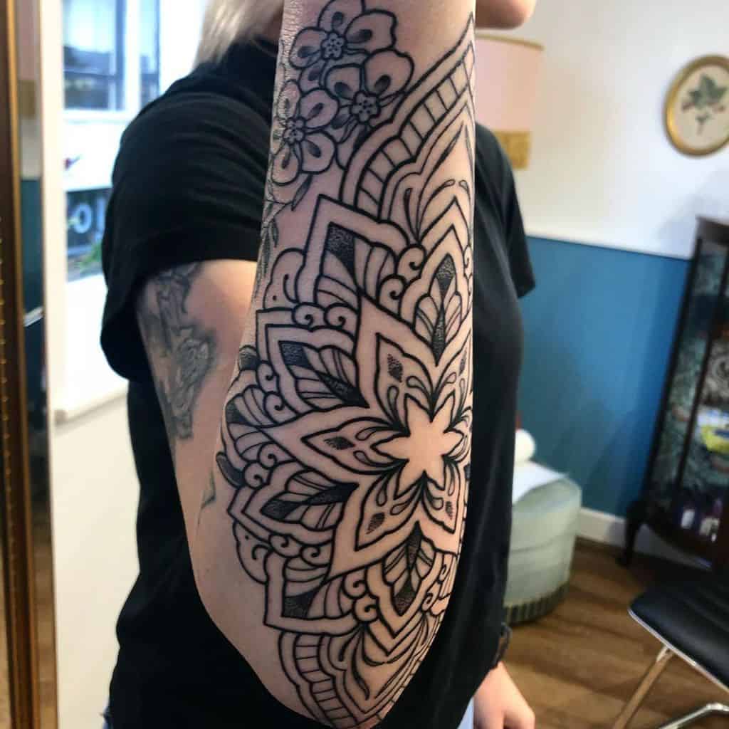 An intricate mandala tattoo covers a person's forearm, featuring floral and geometric patterns in black ink
