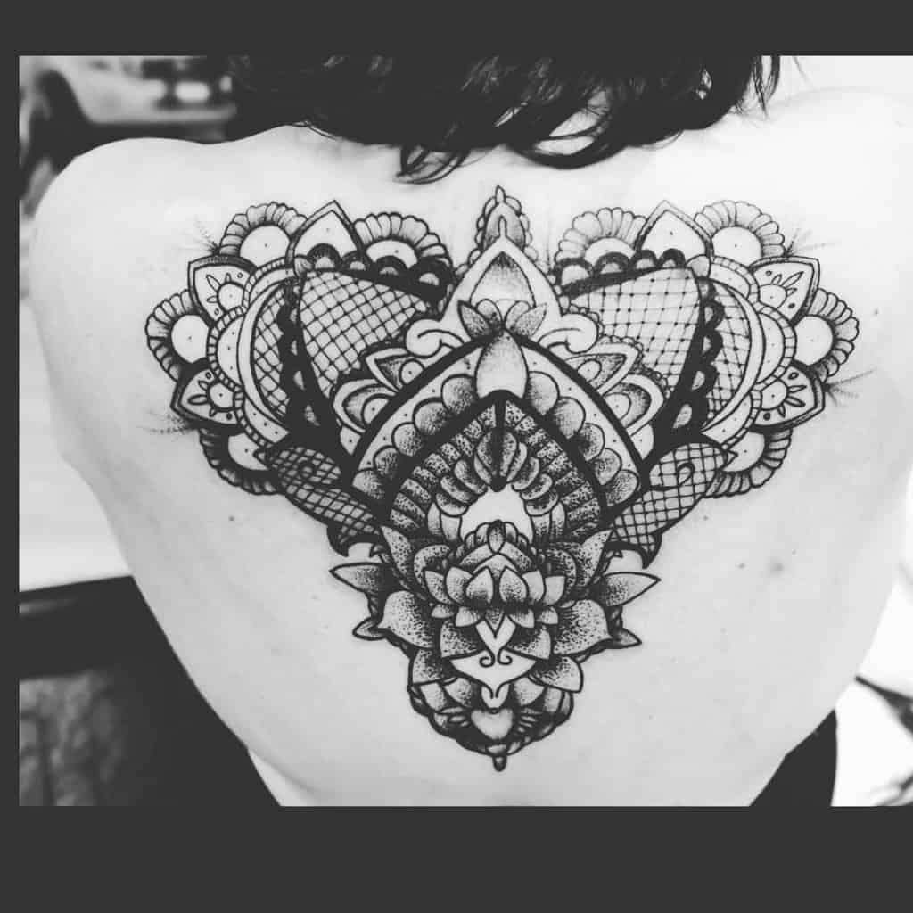 Intricate blackwork back tattoo featuring symmetrical lace patterns, mandala elements, and ornamental lotus flower details.