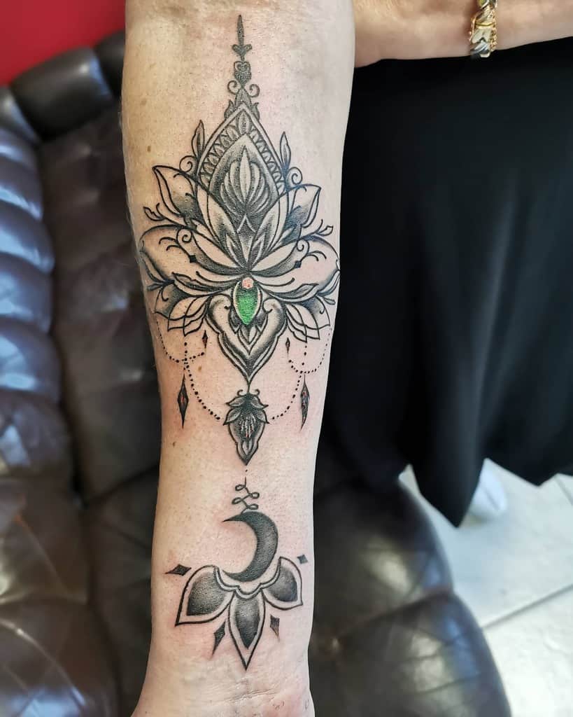 Intricate forearm tattoo featuring floral and geometric designs with an emerald green stone