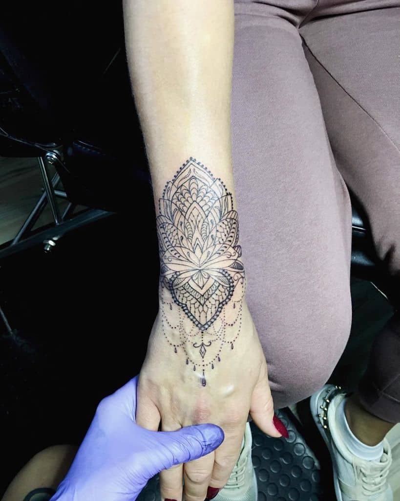 Elegant mandala-style lace tattoo on the wrist and hand, featuring intricate patterns and delicate dotwork with ornamental details.