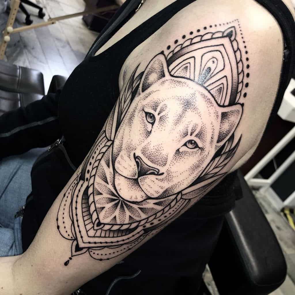 Bold black and grey lioness tattoo on the upper arm, featuring intricate dotwork, mandala patterns, and geometric elements for a striking look.