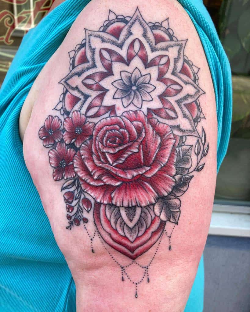 Intricate tattoo with a red rose, flowers, and a mandala pattern on a woman's upper arm