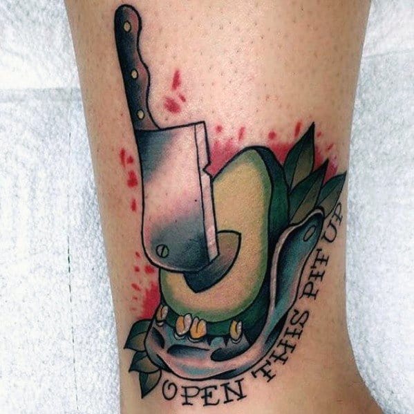 Edgy avocado tattoo with a cleaver chopping through it, surrounded by blood splatters, a snake, and the phrase “OPEN THIS PIT UP.”