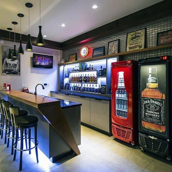 Modern home bar with high stools, pendant lights, liquor shelves, and beverage coolers in a cozy setting