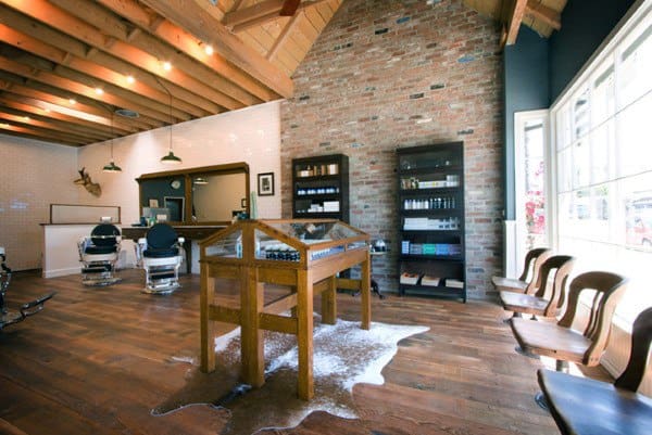Rustic barber shop with exposed beams, brick wall, wooden furniture, and large display table.