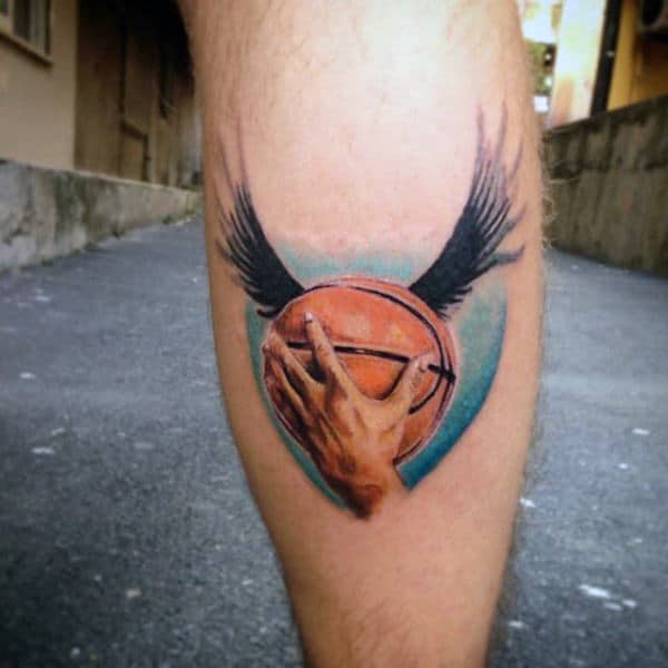 Tattoo of a hand holding a basketball with wings on a calf