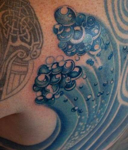 Tattoo of waves with a cluster of bubbles rising from the water, featuring bold blue shading and intricate detailing that creates a dynamic, flowing design.