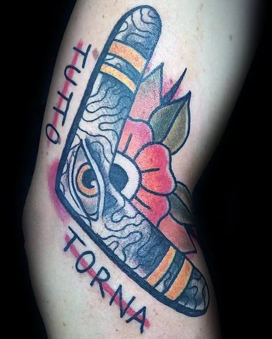 Boomerang tattoo with an eye, red flower, and swirling texture, surrounded by the words TUTTO TORNA on the upper arm.