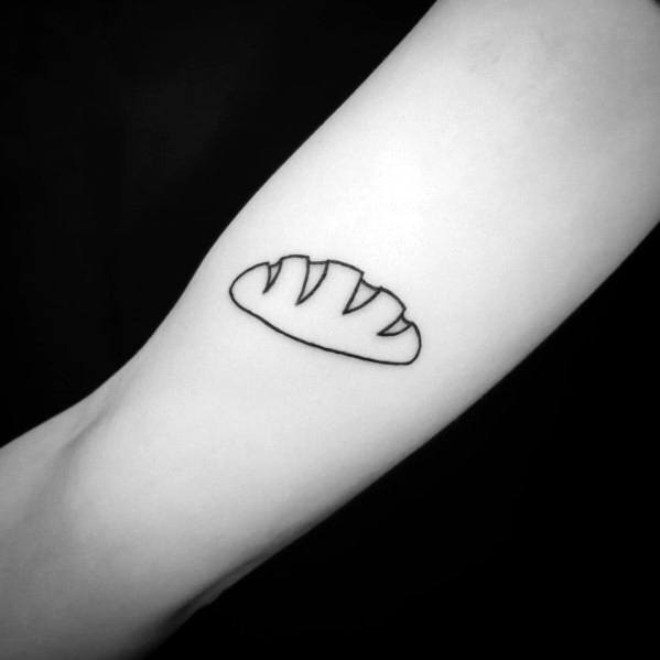 Minimalist black ink tattoo of a simple bread loaf outline with slashes, featuring clean lines for a subtle and modern design.