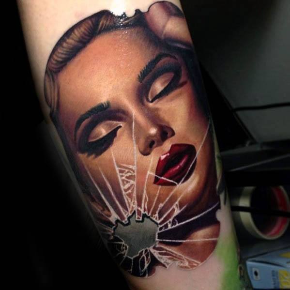 Colorful tattoo of a glamorous woman’s face with closed eyes and shattered glass over her cheek, creating a bold contrast of beauty and destruction.