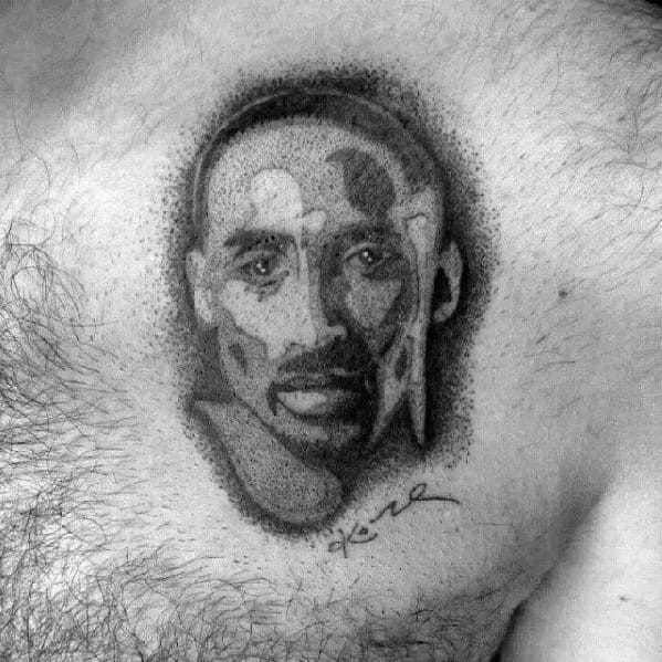 A black and white tattoo of Kobe Bryant's face, designed with a unique, stippled dot work technique, along with his signature beneath the image.