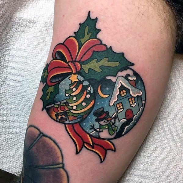 Colorful Christmas ornament tattoo featuring a decorated tree, snowy cottage, holly leaves, and a red ribbon, creating a festive holiday design.